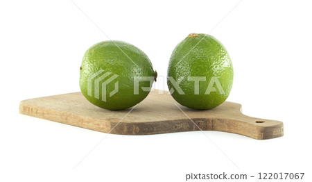 Two fresh limes resting on a wooden cutting board 122017067
