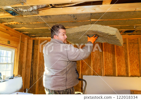 Contractor is lifting, placing insulation material onto ceiling of wooden room during home improvement project. Contractor is lifting, placing insulation material onto ceiling of wooden room during home improvement project. 122018334