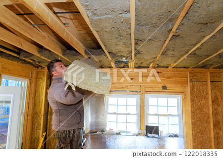 Man works on installing insulation at ceiling in residential property during renovations Man works on installing insulation at ceiling in residential property during renovations 122018335
