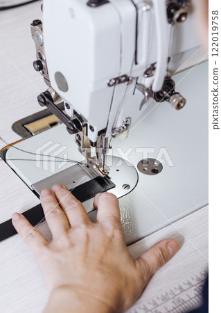 Tanners hands sew leather strips on a sewing machine indoor, vertical image, close-up. 122019758