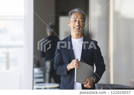 A senior businessman in his 60s smiling at the camera with a laptop 122020037