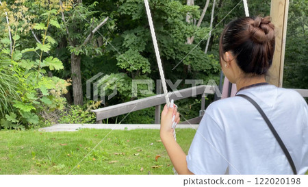 Back view of a young Japanese woman playing on a swing in a natural mountain park Back view of a young Japanese woman playing on a swing in a natural mountain park 122020198