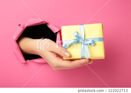 Female hand with gift box punching through the pink paper Female hand with gift box punching through the pink paper 122022713