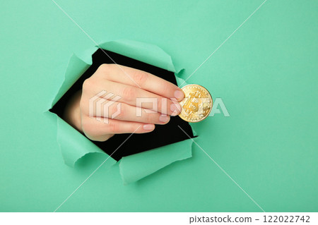 Female hand with coin of bitcoin punching through the paper Female hand with coin of bitcoin punching through the paper 122022742
