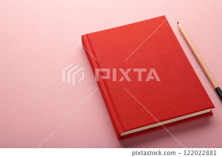Red notebook with pen on pink background. Top view 122022881