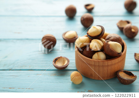 Peeled macadamia nuts in wooden bowl on blue background. 122022911