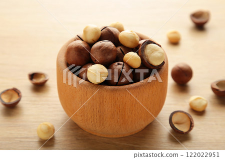 Peeled macadamia nuts in wooden bowl on light background. Peeled macadamia nuts in wooden bowl on light background. 122022951