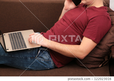 Young man working at home using laptop and talking on the phone. 122023016