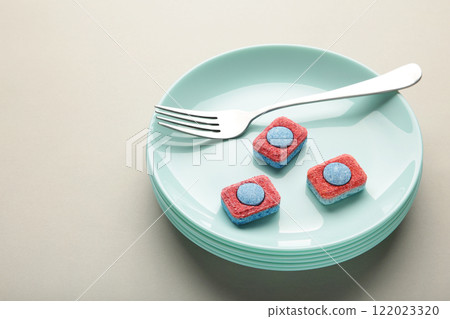 Dishwasher detergent tablet with fork and dishes on blue background. 122023320