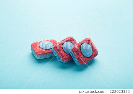 Red and blue tablets for dishwashing machine. Detergents for home hygiene. Dishwasher capsules on blue background. Red and blue tablets for dishwashing machine. Detergents for home hygiene. Dishwasher capsules on blue background. 122023323