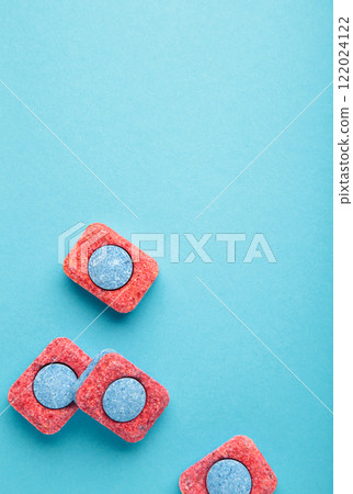 Red and blue tablets for dishwashing machine. Detergents for home hygiene. Dishwasher capsules on blue background. Red and blue tablets for dishwashing machine. Detergents for home hygiene. Dishwasher capsules on blue background. 122024122
