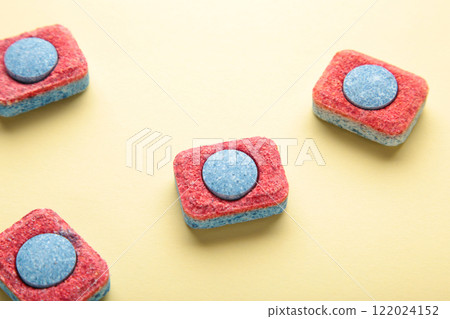 Red and blue tablets for dishwashing machine. Detergents for home hygiene. Dishwasher capsules on yellow background. 122024152