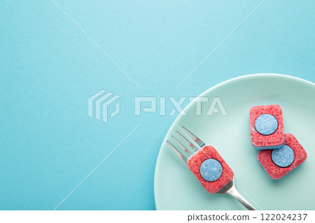 Dishwasher detergent tablet with fork and dishes on blue background. Space for text Dishwasher detergent tablet with fork and dishes on blue background. Space for text 122024237