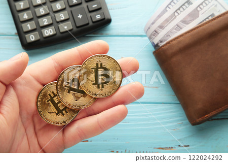 Bitcoin coin in man hands and cash with calculator on blue wooden background. Bitcoin growthand investment concept. Bitcoin coin in man hands and cash with calculator on blue wooden background. Bitcoin growthand investment concept. 122024292