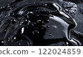 Black liquid with drops of water on top of it. The liquid is dark and has a shiny appearance 122024859