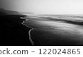 Black and white photo of a beach with a foggy sky in the background. The water is calm and the beach is empty 122024865