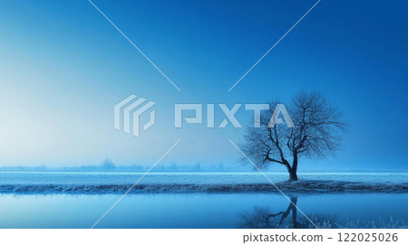 Tree stands alone in a field of snow. The sky is a deep blue color. The scene is peaceful and serene 122025026