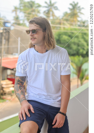 A man in sunglasses and a white tshirt stands on a balcony 122025769
