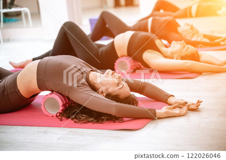 Athletic women doing fascia exercises on the floor with a foam roller massage tool to relieve back tension and relieve muscle pain. The concept of physiotherapy and stretching training 122026046