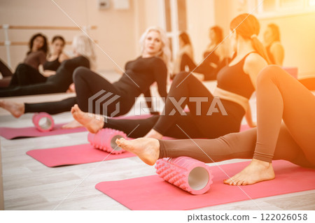 Athletic women doing fascia exercises on the floor with a foam roller massage tool to relieve back tension and relieve muscle pain. The concept of physiotherapy and stretching training 122026058