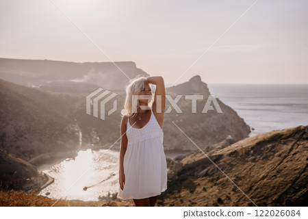 A blonde woman stands on a hill overlooking the ocean. She is wearing a white dress and she is enjoying the view. A blonde woman stands on a hill overlooking the ocean. She is wearing a white dress and she is enjoying the view. 122026084