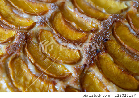 A dessert made of sliced peaches is on a wooden cutting board. The dessert is covered in sugar and looks delicious. A dessert made of sliced peaches is on a wooden cutting board. The dessert is covered in sugar and looks delicious. 122026157