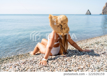 Beach Relaxation woman in hat sits on a pebble beach enjoying the sunshine. The concept of travel, vacation at sea 122026159