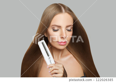 Stylish brunette lady with straight hair holding straightening iron on white background.  122026385