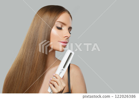 Beautiful brunette lady with straight hair holding straightening iron on white background. 122026386