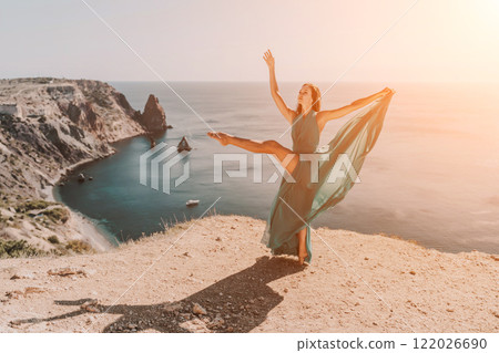 Woman green dress sea. Female dancer posing on a rocky outcrop high above the sea. Girl on the nature on blue sky background. Fashion photo. Woman green dress sea. Female dancer posing on a rocky outcrop high above the sea. Girl on the nature on blue sky background. Fashion photo. 122026690