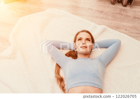 Top view portrait of relaxed woman listening to music with headphones lying on carpet at home. She is dressed in a blue tracksuit. Top view portrait of relaxed woman listening to music with headphones lying on carpet at home. She is dressed in a blue tracksuit. 122026705