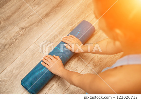 Woman hands rolled up yoga mat on gym floor in yoga fitness training room. Home workout woman close up hands rolling foam yoga gym mat. Woman barefoot home workout sportive healthy lifestyle concept Woman hands rolled up yoga mat on gym floor in yoga fitness training room. Home workout woman close up hands rolling foam yoga gym mat. Woman barefoot home workout sportive healthy lifestyle concept 122026712