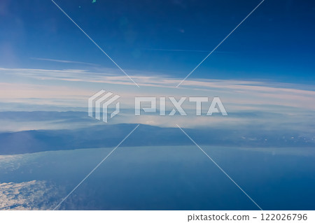 Aerial view from airplane window above green ground. View from the airplane window with beautiful clouds at sunrise. Earth and sky as seen through window of an airplane. High quality photo 122026796