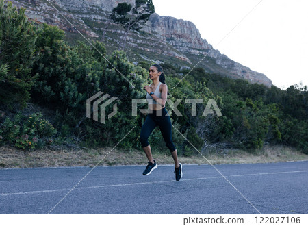 Full length of a young slim female practicing running outdoors on an abandoned road. Woman athlete jogging outdoors in natural park.  122027106