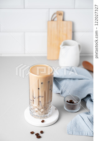 Cold latte coffee in a tall glass with alternative milk on a light table on a white brick background 122027327