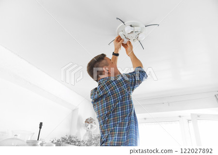 A man in a plaid shirt replacement of light bulbs in a ceiling lamp at home 122027892