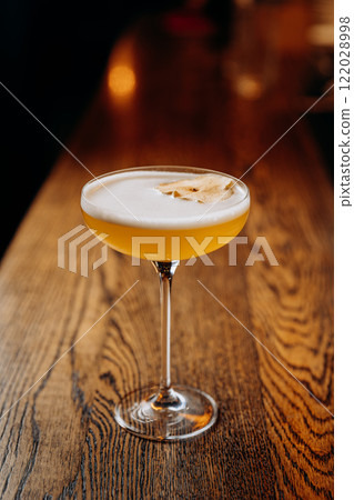 Exquisite yellow cocktail garnished with dried apple on bar counter, perfect for mixology themes Exquisite yellow cocktail garnished with dried apple on bar counter, perfect for mixology themes 122028998