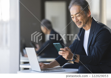 Senior businessman looking at smartphone screen while working on computer 122029053