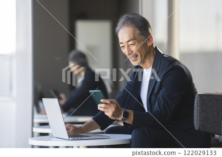 Senior businessman looking at smartphone screen while working on laptop 122029133