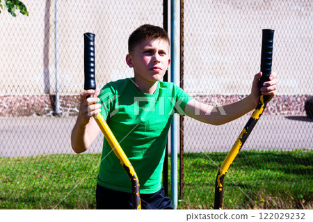 Boy exercising outdoors on a sunny day using a rusty yellow fitness machine. Boy exercising outdoors on a sunny day using a rusty yellow fitness machine. 122029232