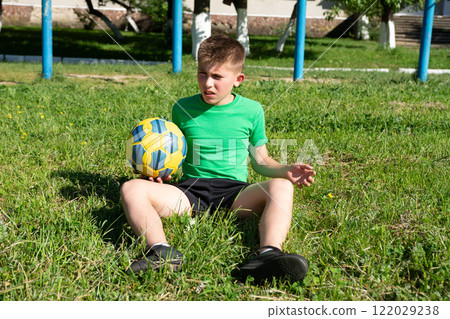 Boy rests on grass after a soccer game, holding his ball. He looks tired but content. Boy rests on grass after a soccer game, holding his ball. He looks tired but content. 122029238