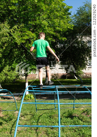 Boy playfully walks across a climbing frame outdoors on a sunny day. 122029240