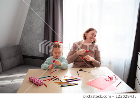 Happy young Caucasian mother teaches her little daughter how to cut hearts out of paper. The concept of Mother's Day and Valentine's Day 122029433