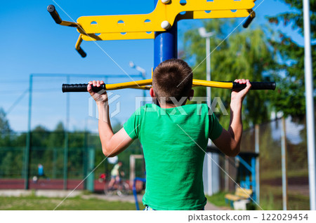 Boy doing pull-ups on outdoor fitness equipment. Sunny day, active lifestyle. Boy doing pull-ups on outdoor fitness equipment. Sunny day, active lifestyle. 122029454