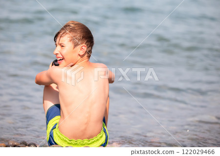 A little boy is relaxing by the sea and sitting with his back to the camera. A little boy is relaxing by the sea and sitting with his back to the camera. 122029466