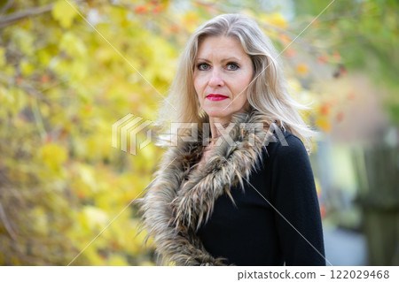 A beautiful blonde elderly woman on the background of an autumn park. An adult woman of fifty years old. 122029468