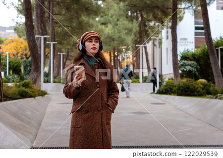 Mid shot of a beautiful young Caucasian woman in a hat and coat with headphones listening to music and using smartphone. Concept of psychology and relax 122029539