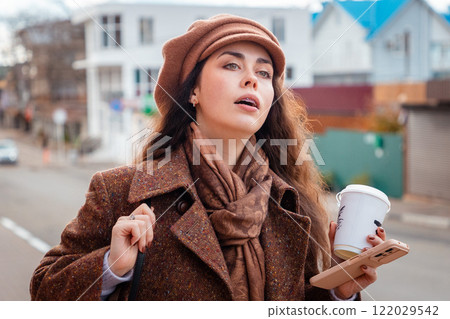 Portrait of young Caucasian woman is walking around the city with cup of coffee. Business and trip. Concept of freedom and city lifestyle Portrait of young Caucasian woman is walking around the city with cup of coffee. Business and trip. Concept of freedom and city lifestyle 122029542