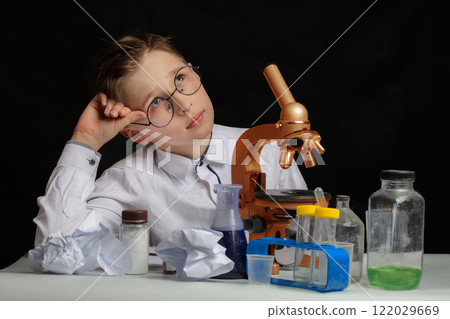 A boy scientist researcher with a microscope is thinking about ideas in the laboratory. Surprise in the laboratory. Science and education. 122029669
