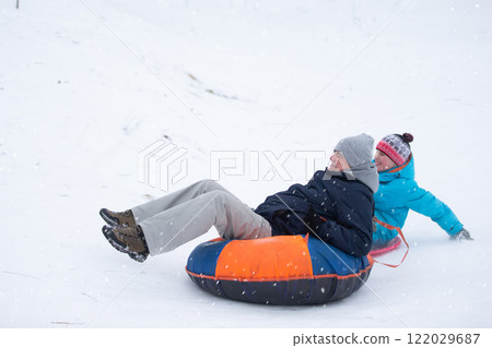 Dad and son roll down a snow slide on a tubing. Dad and son roll down a snow slide on a tubing. 122029687
